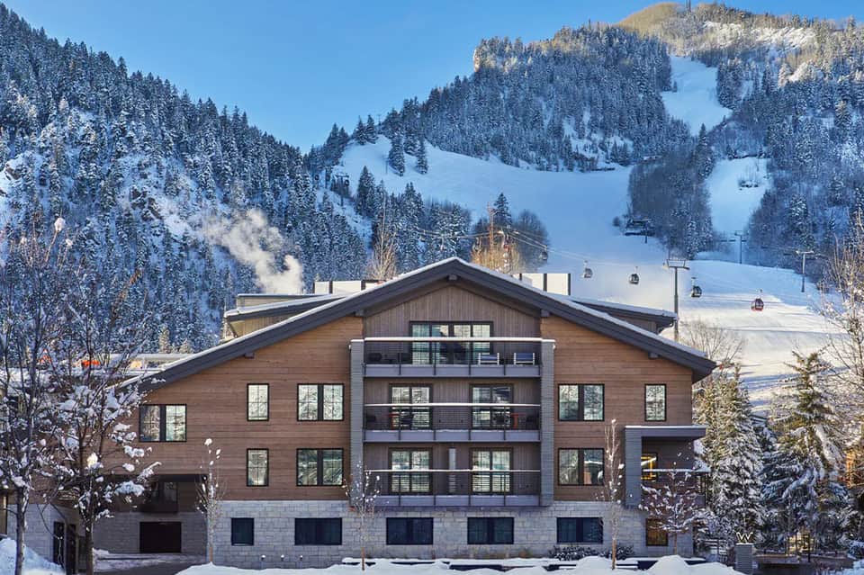 Modern ski resort lodge with wood and stone exterior against snow-covered mountains and ski slopes