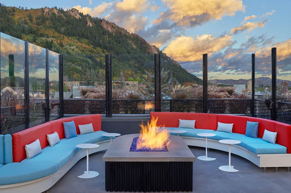 Modern fire pit lounge with curved red and blue seating, mountain and sunset views