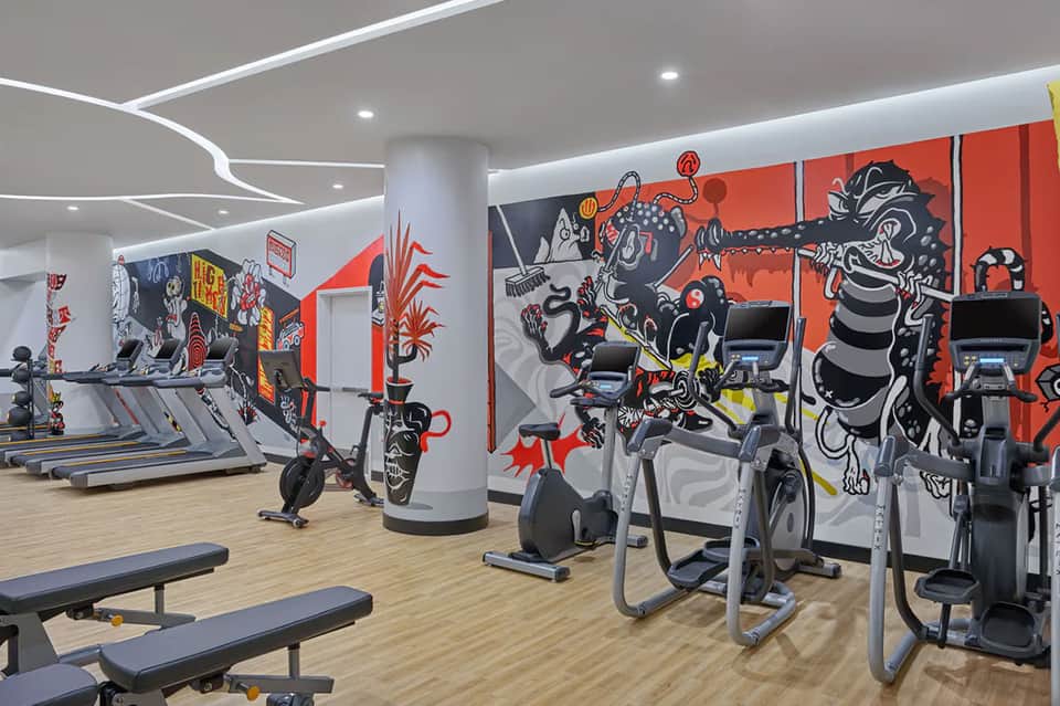 Modern fitness center with treadmills, exercise bikes, and vibrant red and black street art mural