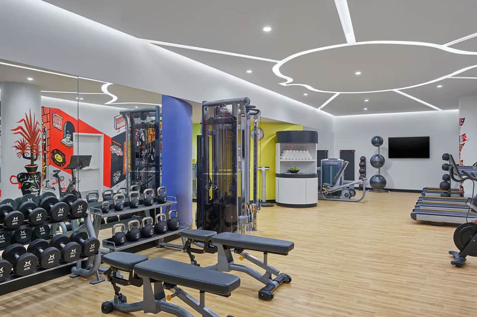 Modern fitness center with colorful accent walls, weight rack, exercise machines, free weights, and contemporary ceiling design