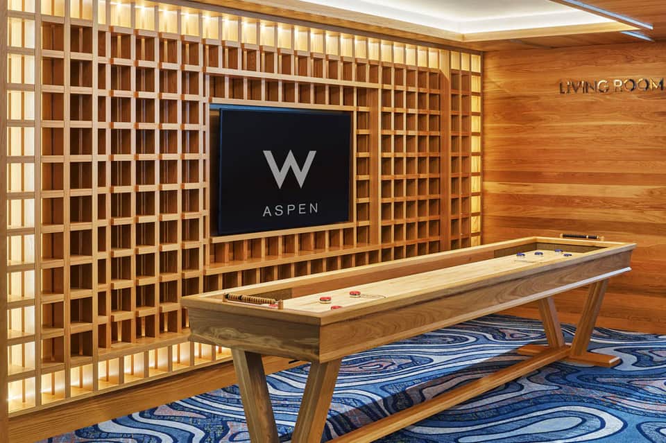 Hotel game room with air hockey table, TV displaying W Aspen logo, and wooden wall paneling