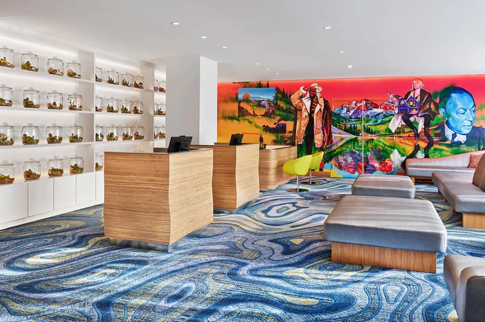 Modern hotel lobby with colorful abstract wall art, wooden reception desk, and blue patterned carpet