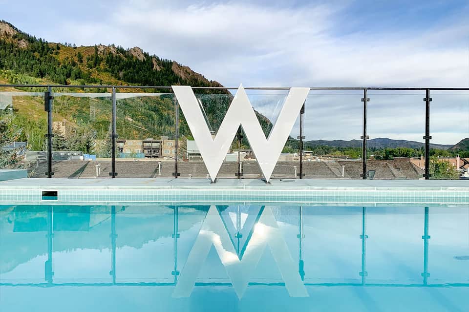W hotel pool with large white logo, glass railings, and mountain landscape backdrop