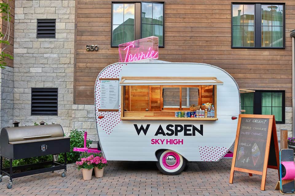 Pink and white vintage ice cream trailer at resort courtyard with neon sign