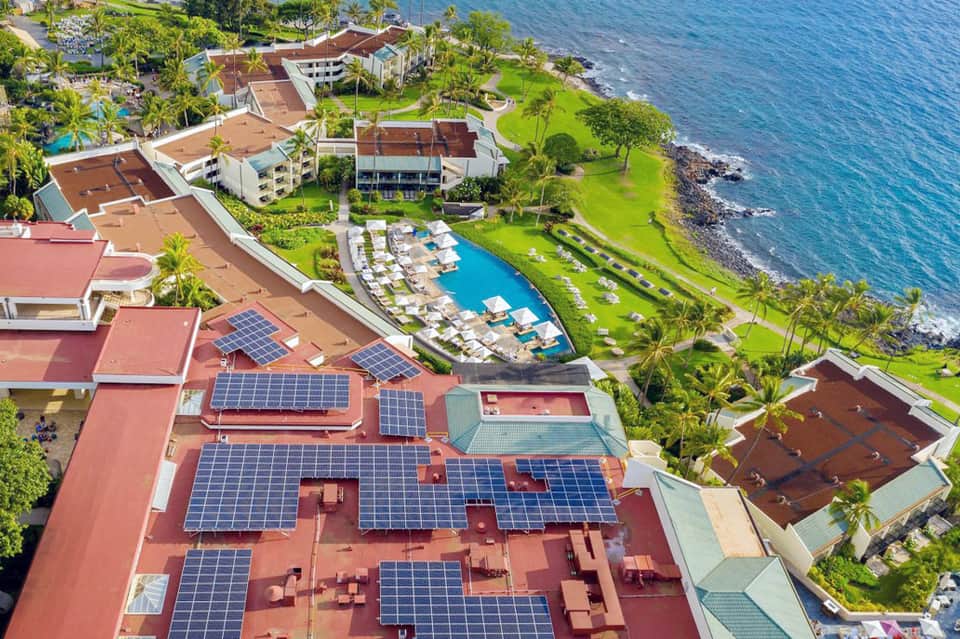 Hillside oceanfront resort with solar panels, pools, lush landscaping overlooking rocky coastline