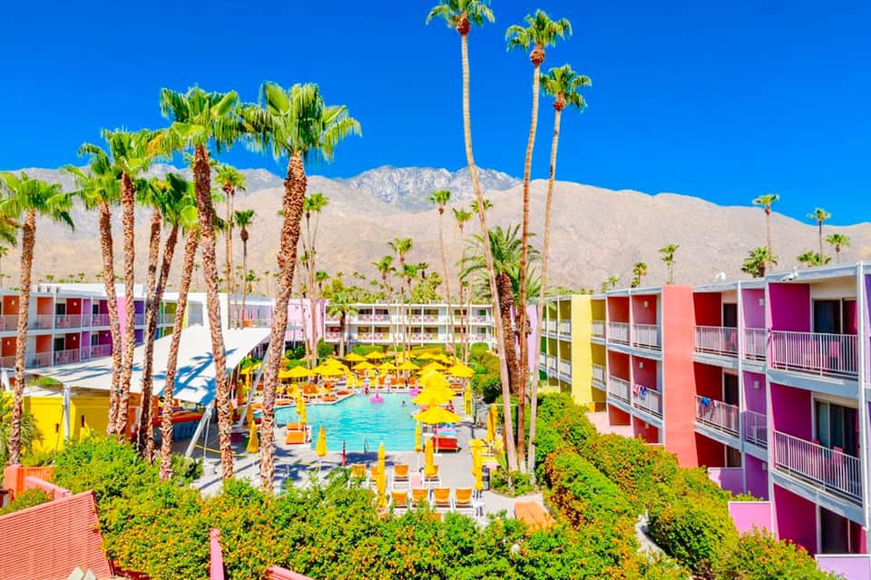 Colorful resort courtyard with bright buildings surrounding a turquoise pool and palm trees