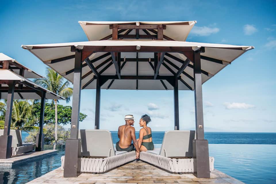 Couple relaxing in beachfront cabana with ocean view and white lounge seating