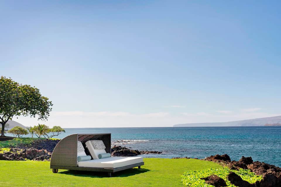 Luxury outdoor daybed on manicured lawn overlooking rocky coastline and ocean