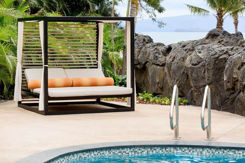 Modern daybed with black frame and white cushions overlooking pool with rock features and ocean view