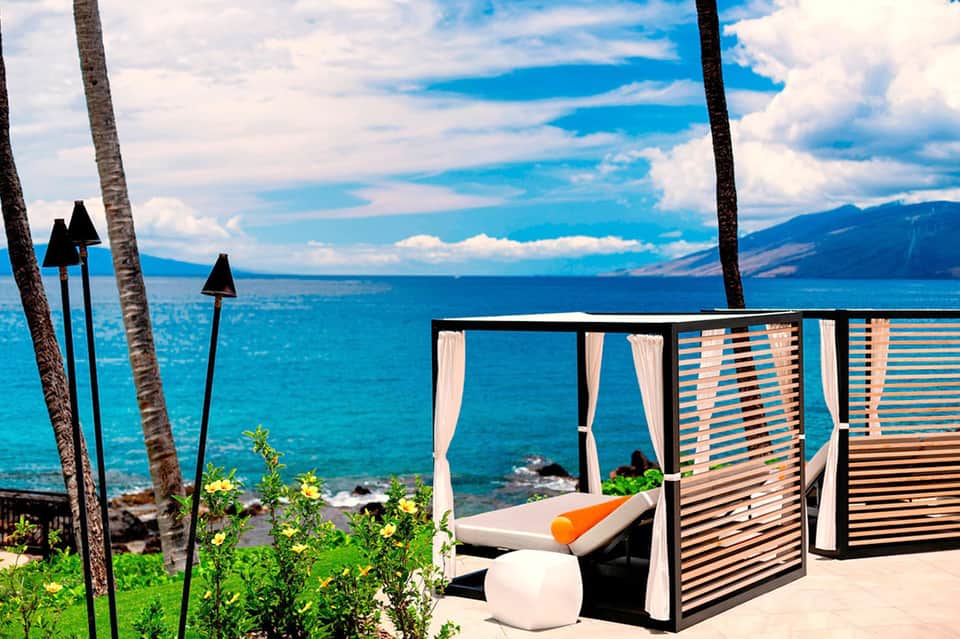 Oceanfront cabana with white curtains, loungers, and blue water vista