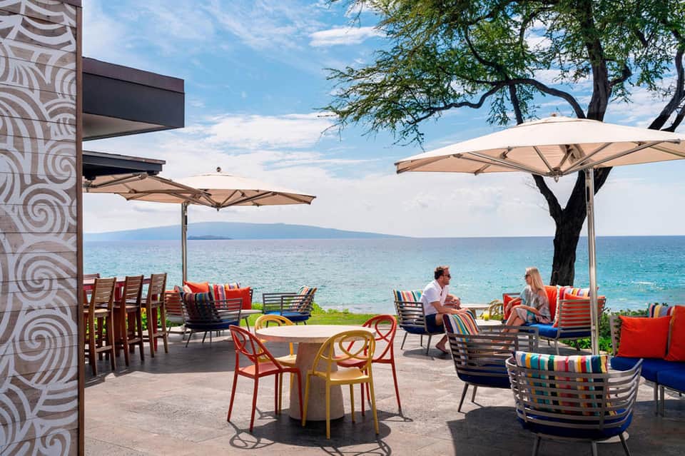 Beachfront terrace with colorful striped chairs, umbrellas, ocean view, and casual dining area