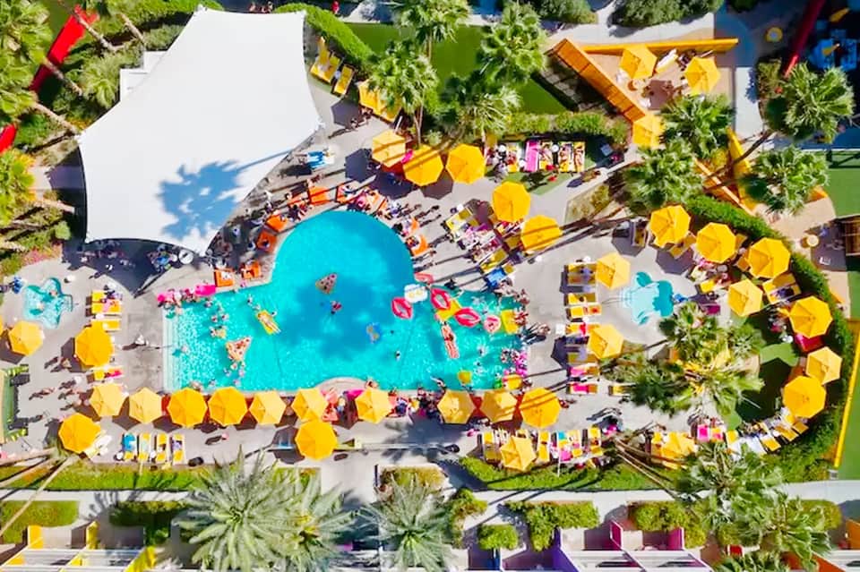 Aerial view of a resort pool with turquoise water, surrounded by yellow umbrellas and lounge chairs
