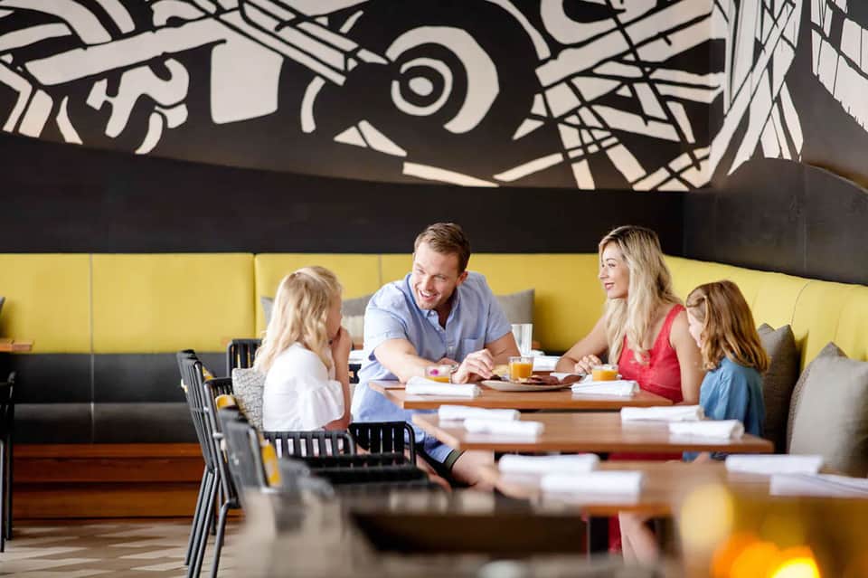 Family dining at modern restaurant with yellow booth seating, artistic ceiling mural, and natural light
