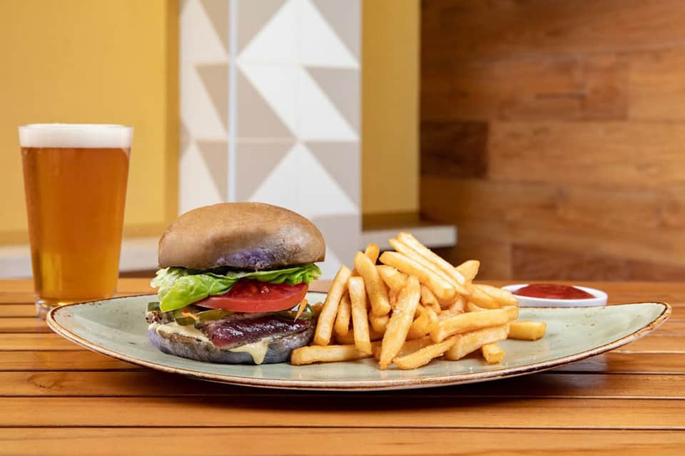 Burger with fries and beer on wooden table in warm-toned dining area