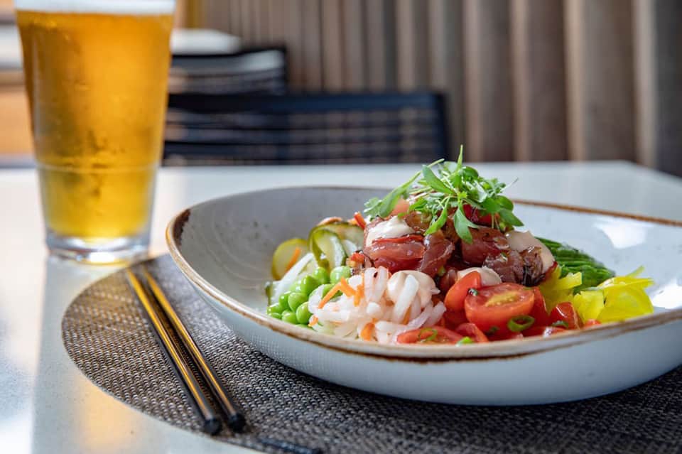Plated Asian noodle dish with fresh vegetables and beer served in modern resort dining setting