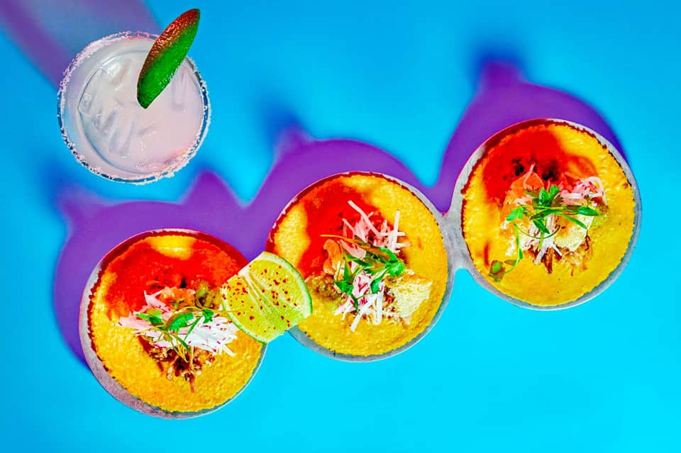 Three colorful tropical bowls with yellow rim, lime garnish, and pink drink on blue background
