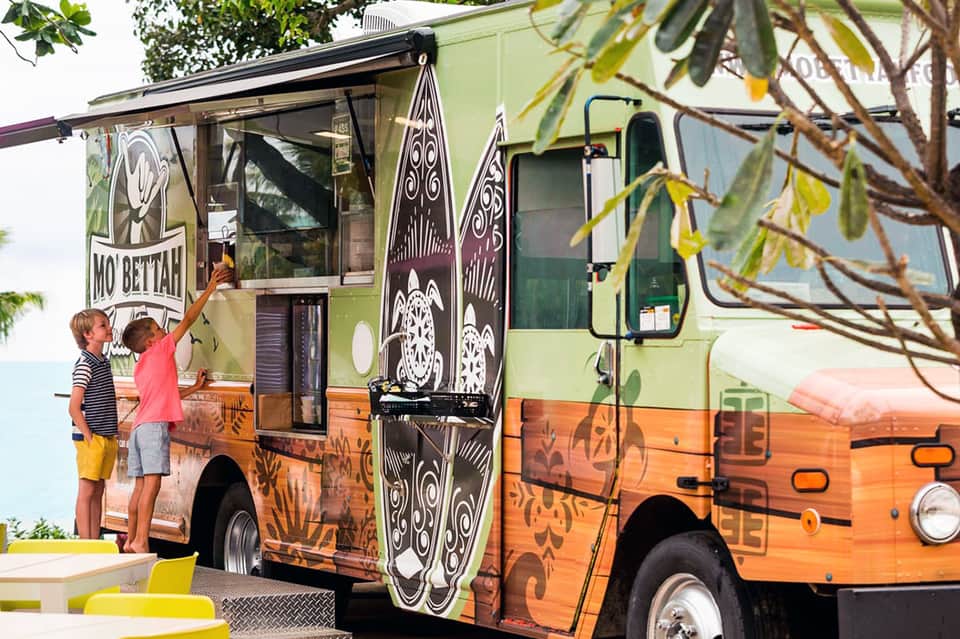 Food truck with decorative design and children ordering at service window in outdoor setting