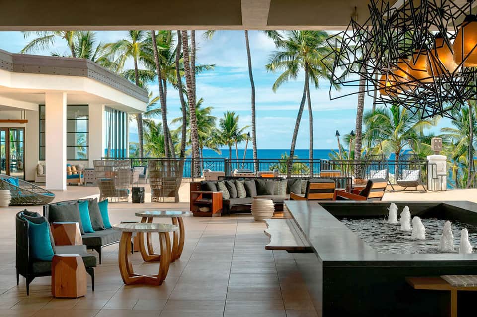 Modern oceanfront terrace with lounge seating, fountain, palm trees, and ocean views