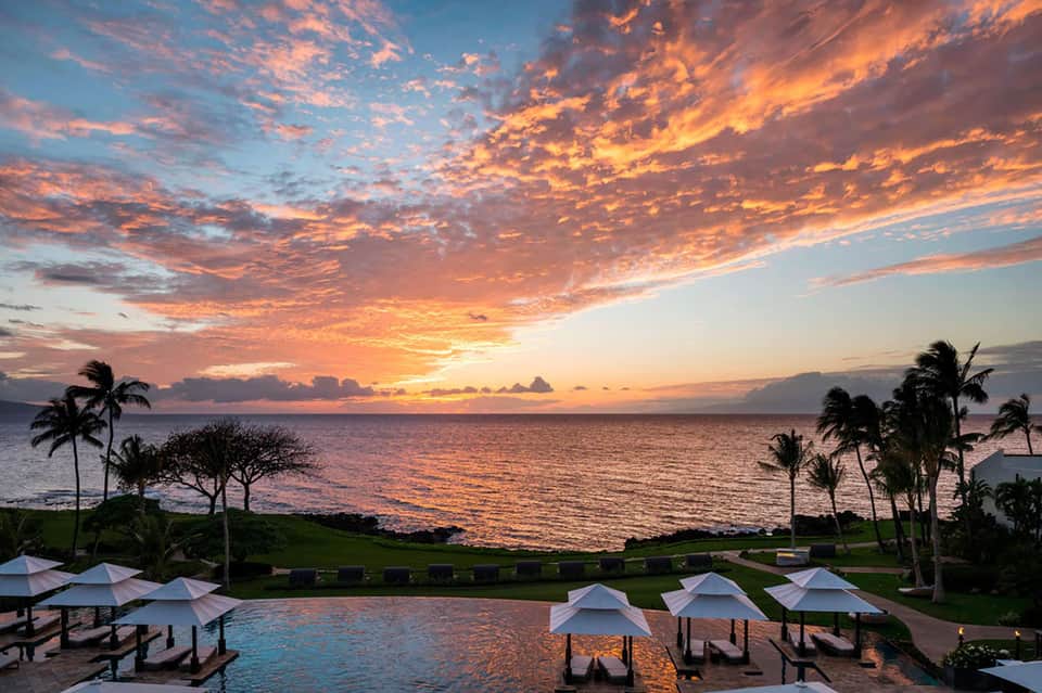 Oceanfront resort pool at golden hour sunset with white umbrellas and palm trees