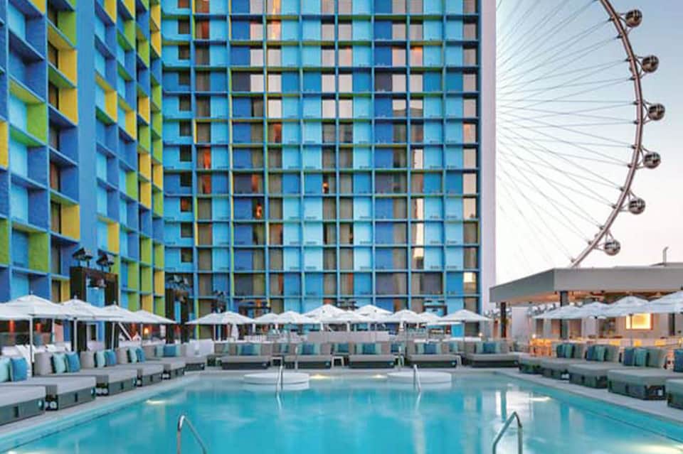 Resort pool deck with colorful building facade, white umbrellas, and London Eye visible