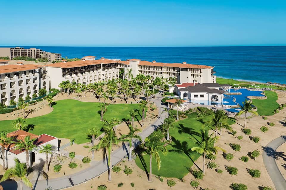 Beachfront resort with white buildings, manicured lawn, pool, and ocean views