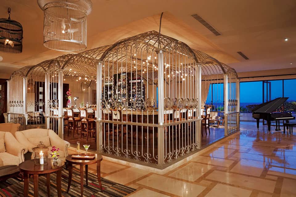 Luxurious dining room with ornate brass bird cage structure and grand piano at dusk