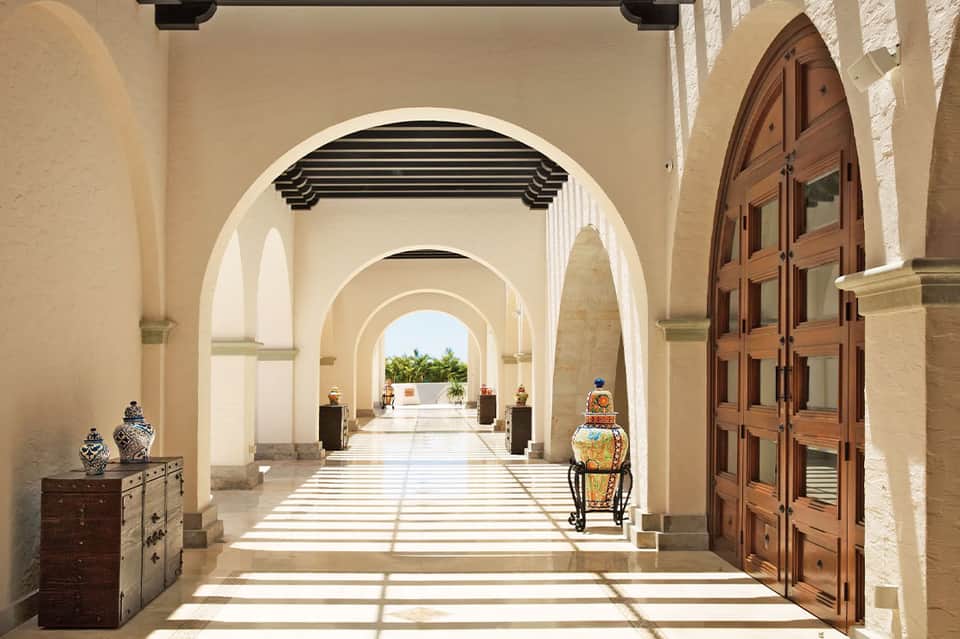Arched hallway with cream columns, wooden doors, and decorative urns