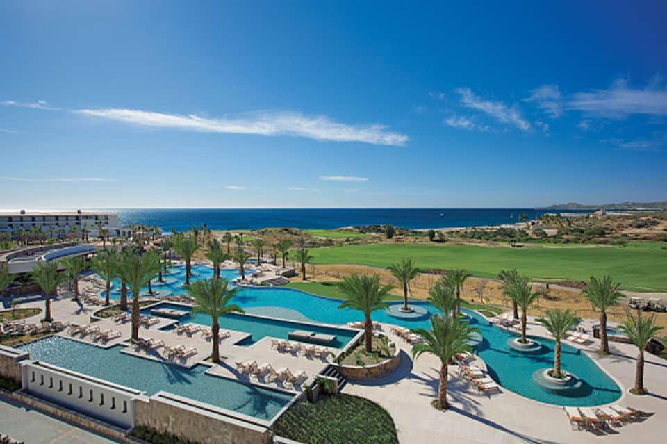 Expansive resort complex with multiple turquoise pools, palm trees, and ocean views