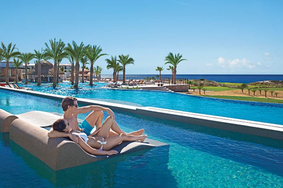 Guests relaxing on floating lounger in resort infinity pool overlooking ocean