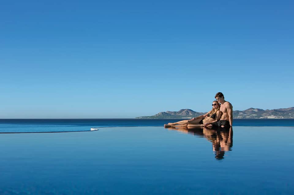 Couple relaxing in infinity pool overlooking mountains and ocean