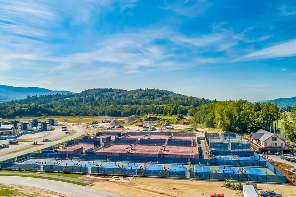 Overhead view of outdoor tennis and pickleball courts surrounded by forested hills and mountains