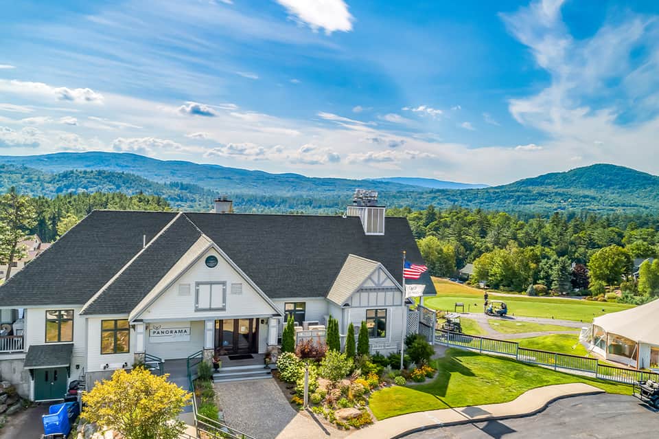 Modern white farmhouse-style building on hillside with mountain and forest landscape background