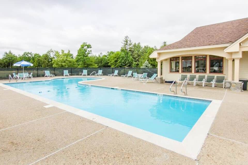 Resort swimming pool with concrete deck, white lounge chairs, and clubhouse building in background