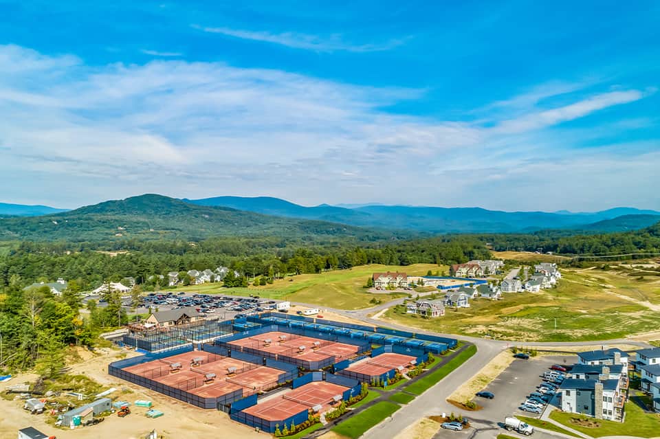 Aerial view of tennis courts and residential community nestled in valley with mountain range backdrop