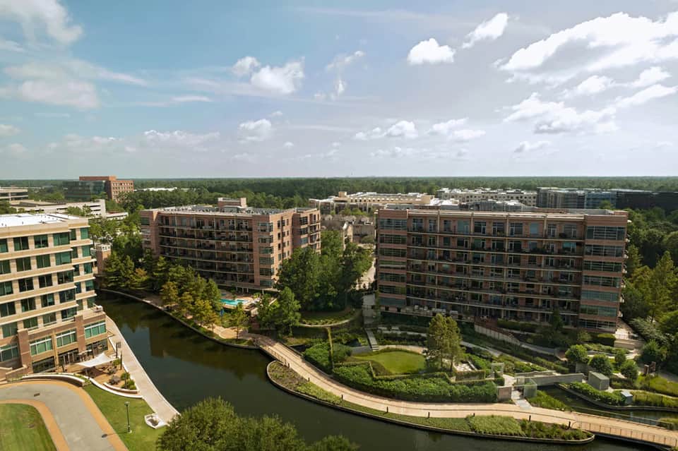 Aerial view of modern residential complex with landscaping along waterway and greenery