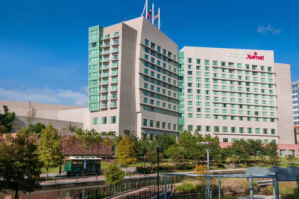 Green and beige Marriott hotel exterior beside waterway with landscaped grounds