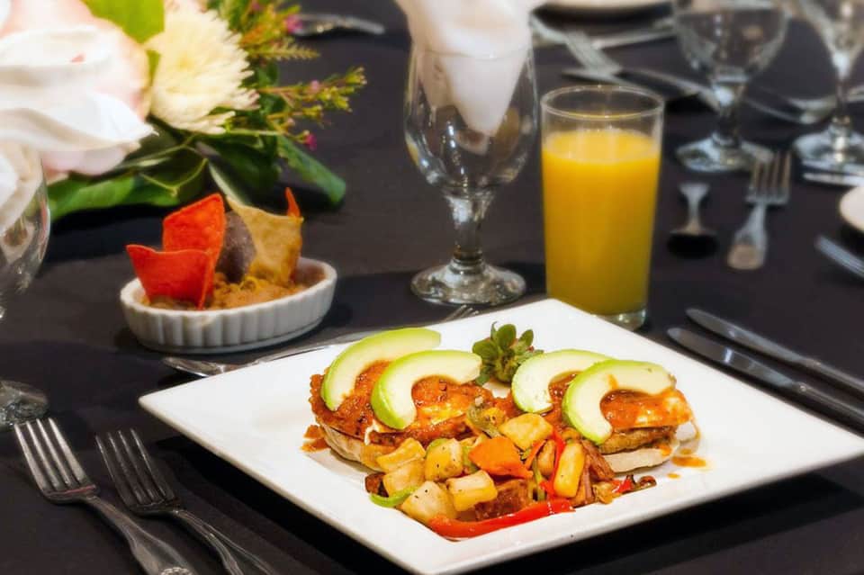 Plated breakfast with avocado toast, roasted vegetables, orange juice, and floral centerpiece