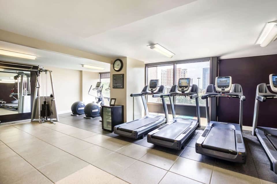 Hotel fitness center with treadmills, exercise equipment, windows overlooking city skyline