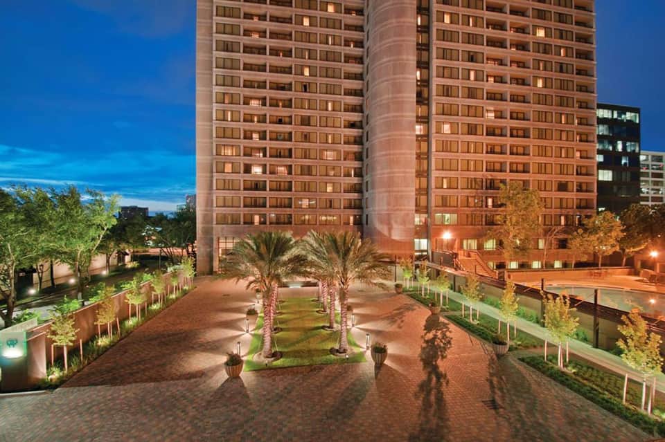 Urban hotel courtyard at night with tall buildings, palm trees, and ambient lighting