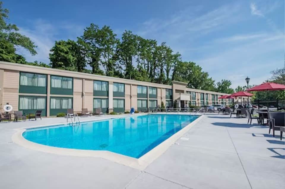 Rectangular swimming pool with modern hotel building and red umbrellas on sunny day