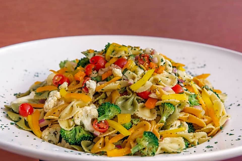 Colorful pasta salad with vegetables, chicken, and fresh herbs on white plate