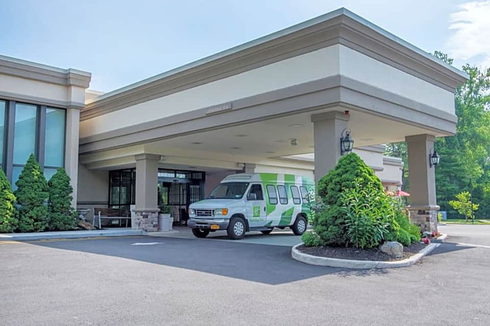 Hotel entrance with modern canopy, landscaping, and vehicle under covered porte-cochere