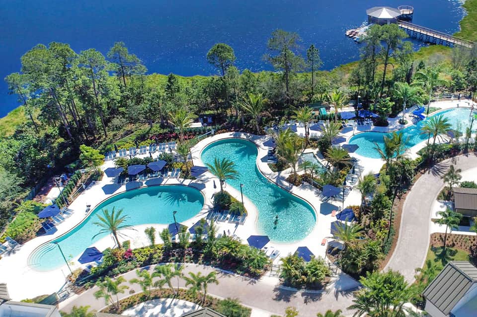 Aerial view of sprawling resort pools with winding lazy river, palm trees, and forested surroundings