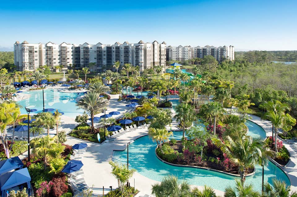 Large resort complex with multiple pools, water features, palm trees, and multi-story hotel buildings