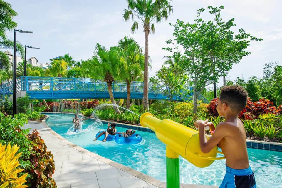 Children playing in resort pool with water slide and lush tropical landscaping