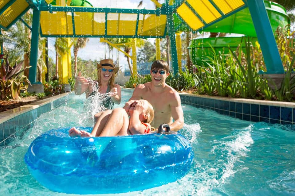 Family enjoying indoor water slide tube in tropical-themed lazy river with bright yellow canopy