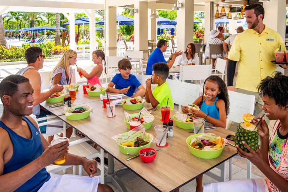 Casual dining area with families and children eating from colorful bowls at long wooden tables