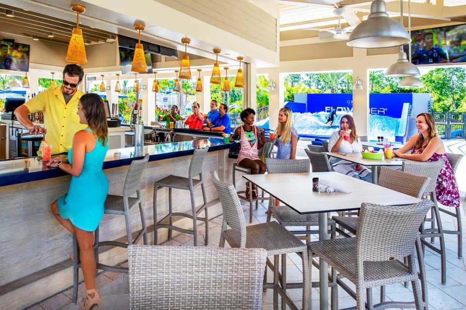 Casual beach bar with bartender, patrons, and ocean view in background