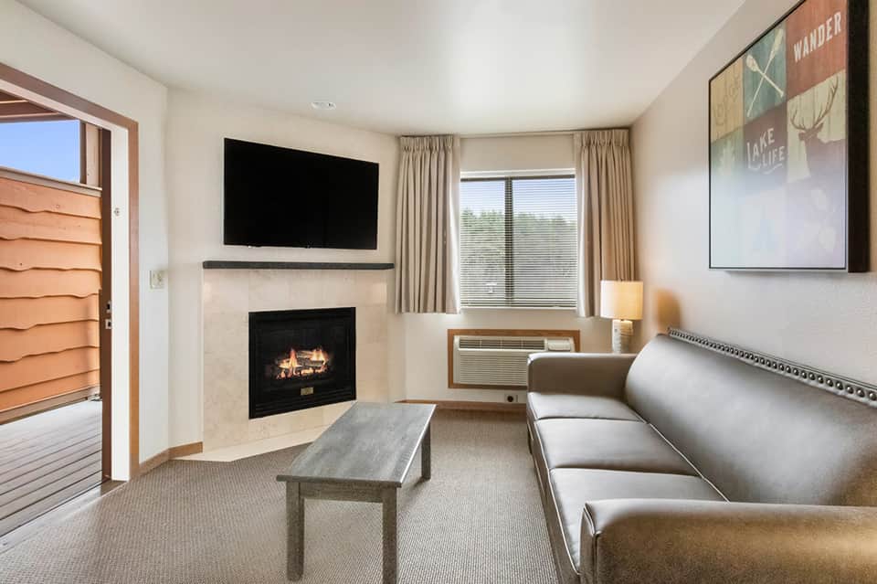 Hotel room with fireplace, flat-screen TV, beige sofa, and glass door to private balcony