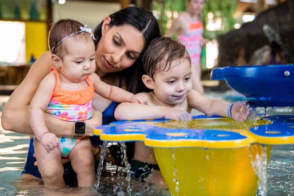 Woman with two toddlers playing in shallow pool water indoors